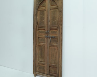 May include: A carved wooden door with a traditional Moroccan design. The door is made of dark wood and has intricate carvings. The door is closed and has a metal latch.