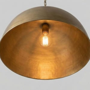May include: A large, dome-shaped pendant light fixture with a warm, brass finish. The interior reflects the light from a single exposed bulb. The fixture hangs from a chain, creating a modern and elegant aesthetic. The light fixture is a statement piece.