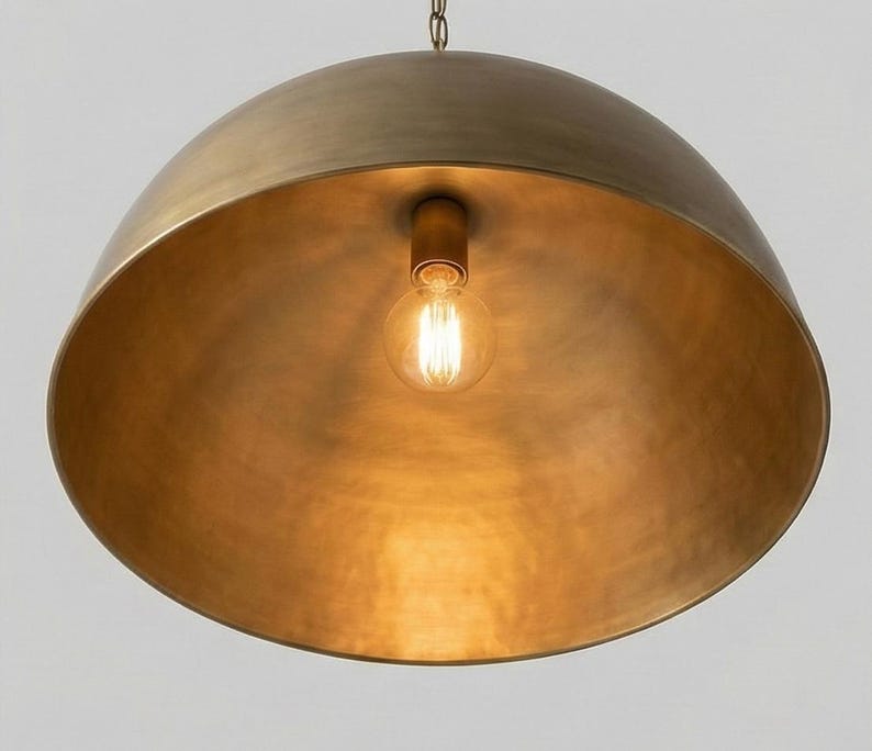 May include: A large, dome-shaped pendant light fixture with a warm, brass finish. The interior reflects the light from a single exposed bulb. The fixture hangs from a chain, creating a modern and elegant aesthetic. The light fixture is a statement piece.