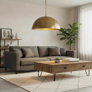 May include: A living room scene featuring a gray sofa with throw pillows, a wooden coffee table, and a large, gold-colored pendant light. A green plant and a patterned rug complete the decor.