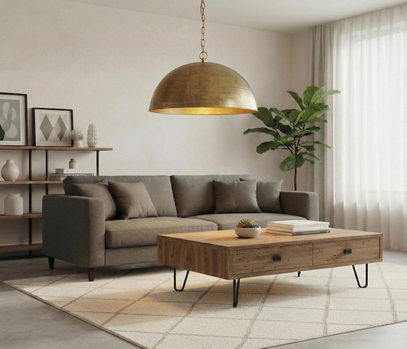 May include: A living room scene featuring a gray sofa with throw pillows, a wooden coffee table, and a large, gold-colored pendant light. A green plant and a patterned rug complete the decor.