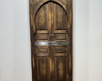 May include: A pair of intricately carved wooden doors with an arched top and metal hardware. The doors are a dark brown color and have a distressed finish.