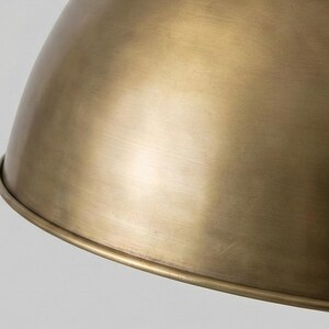 May include: Close-up of a brass-colored pendant light fixture. The light has a rounded, dome-like shape with a slightly textured surface. The fixture has a warm, metallic sheen, reflecting the light.