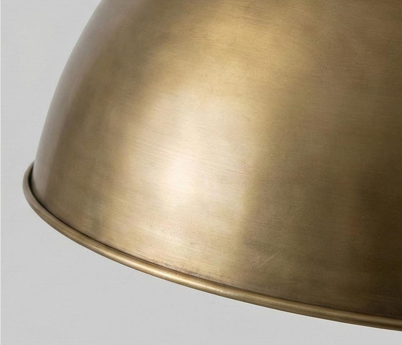 May include: Close-up of a brass-colored pendant light fixture. The light has a rounded, dome-like shape with a slightly textured surface. The fixture has a warm, metallic sheen, reflecting the light.