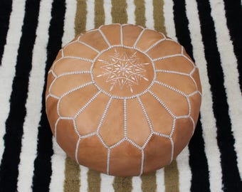 May include: A tan leather pouf with white stitching and a white embroidered star design.