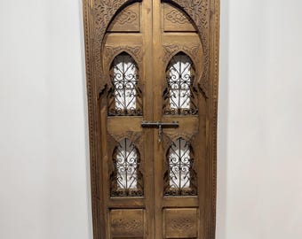 May include: A carved wooden door with an arched top and intricate metalwork details. The door is made of dark wood and has a rustic appearance.