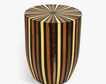 May include: A round wooden stool with a unique striped design. The top of the stool features a sunburst pattern in shades of brown, yellow, and black.