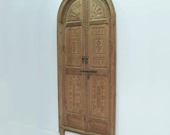 May include: A pair of intricately carved wooden doors with an arched top. The doors are made of light brown wood and feature a variety of geometric and floral designs.