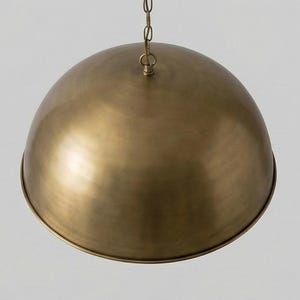 May include: A brass-colored, dome-shaped pendant light fixture. The light hangs from a chain and has a rounded, bowl-like shade. The metal has a warm, antique finish, reflecting light. This ceiling light is suitable for a kitchen or dining room.