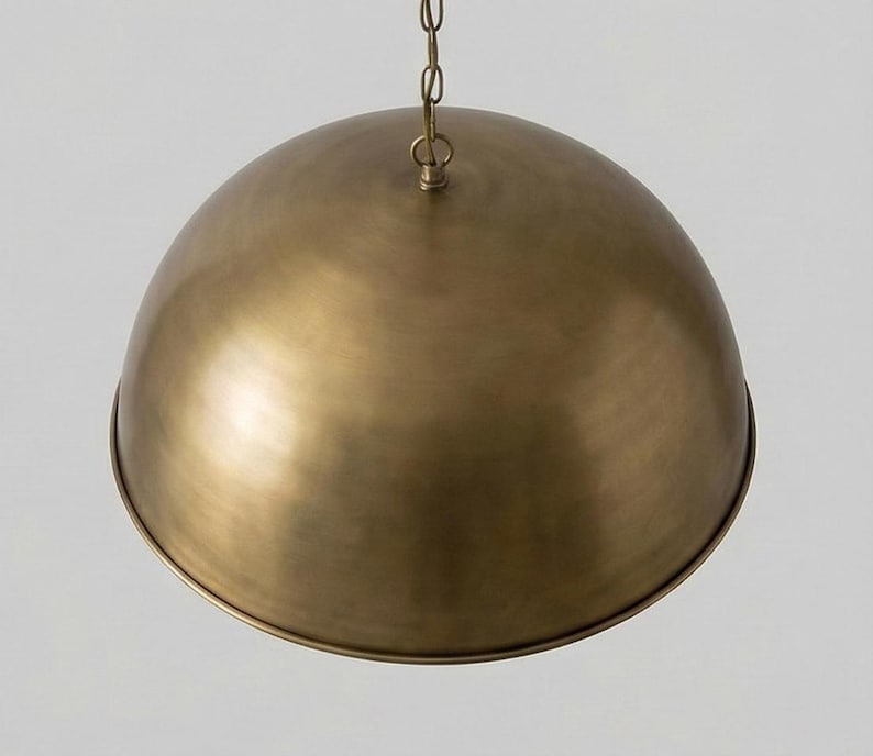 May include: A brass-colored, dome-shaped pendant light fixture. The light hangs from a chain and has a rounded, bowl-like shade. The metal has a warm, antique finish, reflecting light. This ceiling light is suitable for a kitchen or dining room.