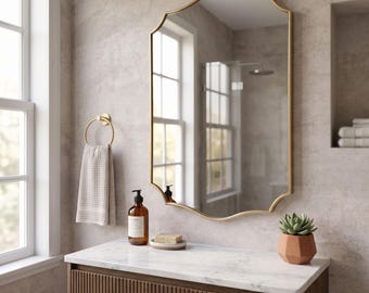 May include: A wall-mounted mirror with a gold-toned scalloped frame. The mirror features a reflective glass surface with a decorative curved edge design. It is positioned above a vanity counter, reflecting the surrounding bathroom interior space.