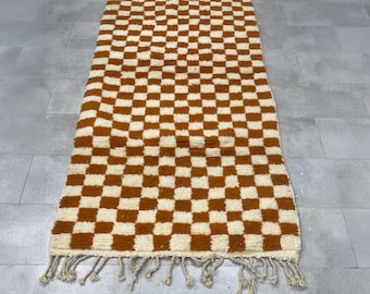 May include: A rectangular rug with a checkerboard pattern in cream and brown. The rug has a fringe on both ends. The rug is made of a soft, textured material.