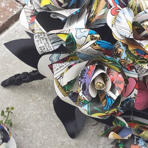 May include: A bouquet of handmade paper flowers made from comic book pages. The flowers are in shades of red, blue, green, and yellow. The bouquet is tied with a black ribbon.