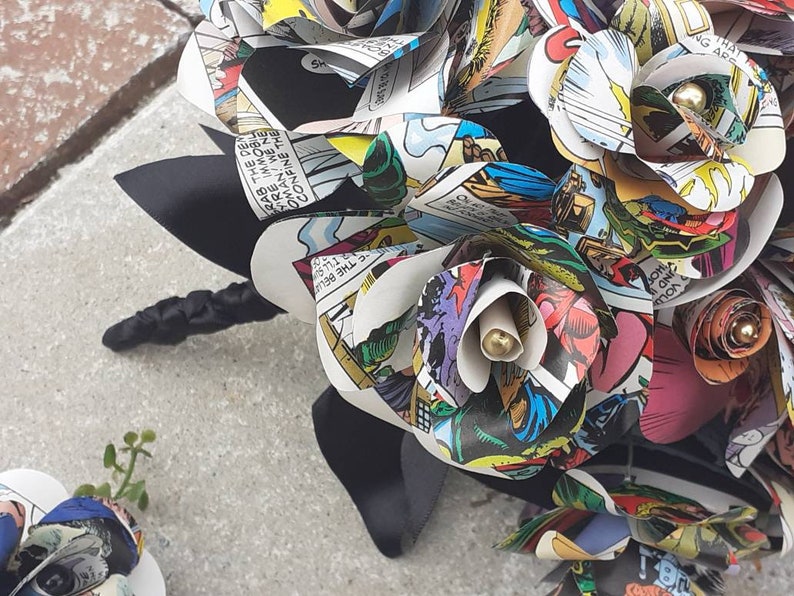 May include: A bouquet of handmade paper flowers made from comic book pages. The flowers are in shades of red, blue, green, and yellow. The bouquet is tied with a black ribbon.