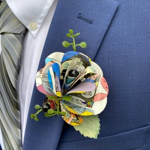 May include: A blue suit jacket with a comic book paper flower boutonniere. The flower is made of colorful comic book pages and has green leaves.