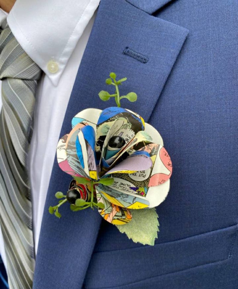 May include: A blue suit jacket with a comic book paper flower boutonniere. The flower is made of colorful comic book pages and has green leaves.