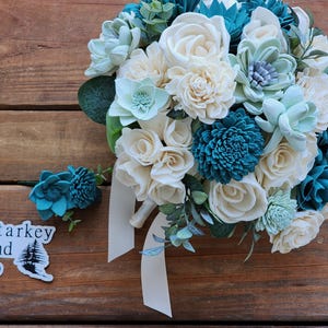 Buquê de casamento com flores de madeira Sola em marfim e azul-petróleo e boutonniere
