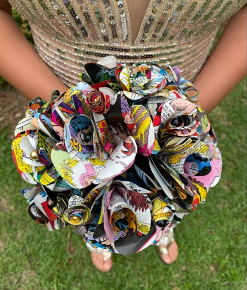 May include: A bouquet of colorful paper roses made from comic book pages. The roses are arranged in a circular shape and are held together with a ribbon. The bouquet is a unique and creative way to celebrate a special occasion.