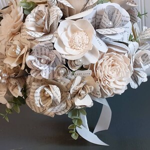 May include: A bouquet of cream-colored paper and wood flowers with a white ribbon. The flowers are made from pages of a book with the text "Last Love" visible.