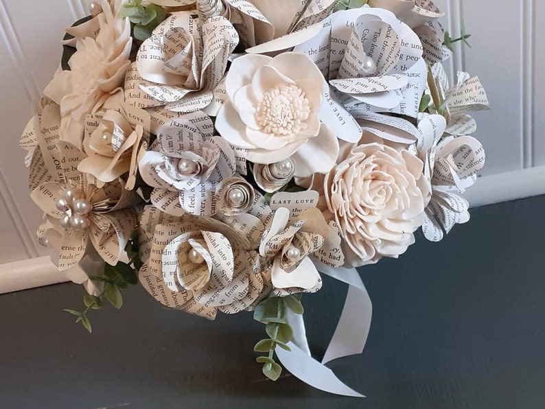 May include: A bouquet of cream-colored paper and wood flowers with a white ribbon. The flowers are made from pages of a book with the text "Last Love" visible.