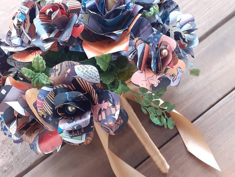 May include: A bouquet of paper roses made from comic book pages. The roses are tied together with a gold ribbon and have small pearl accents.
