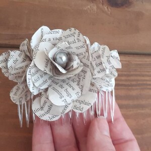 Puede incluir: Un peine para el cabello con una flor de papel blanca con una perla en el centro. La flor est&aacute; hecha de p&aacute;ginas de un libro.