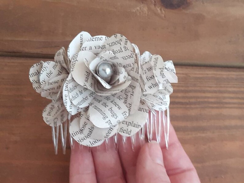 Puede incluir: Un peine para el cabello con una flor de papel blanca con una perla en el centro. La flor est&aacute; hecha de p&aacute;ginas de un libro.