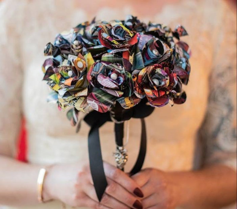 May include: A bouquet of colorful paper roses made from comic book pages. The roses are tied together with a black ribbon and have pearl accents.