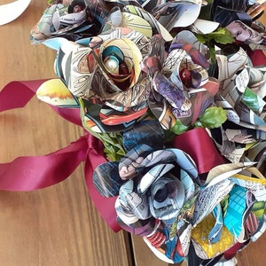 May include: A bouquet of paper roses made from comic book pages. The roses are tied together with a burgundy ribbon.