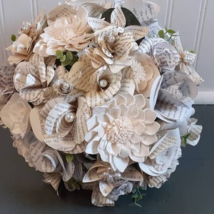 May include: A bouquet of cream-colored paper flowers made from book pages. The bouquet is decorated with small white pearls and green leaves. The text "LOVE NO" is visible on one of the pages.