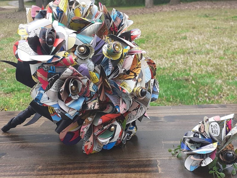 May include: A bouquet of comic book paper roses with black ribbon and a matching boutonniere. The roses are made from colorful comic book pages with black and gold accents.