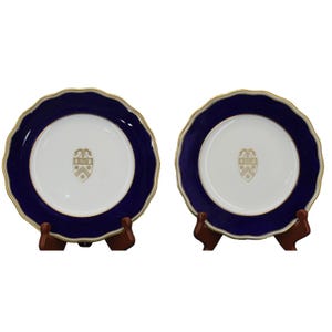 May include: Two blue and gold rimmed porcelain plates with a white center and a gold crest in the center.
