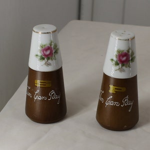 May include: A pair of salt and pepper shakers with a white porcelain top and a brown wooden base. The tops feature a pink rose design and the bases are inscribed with "Tin Can Bay" and "S" and "P" in gold lettering.