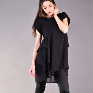 Op de afbeelding: Zwarte gelaagde tuniek top met korte mouwen en leggings. De tuniek heeft een gelaagd ontwerp met een asymmetrische zoom. De leggings zijn nauwsluitend en zwart.