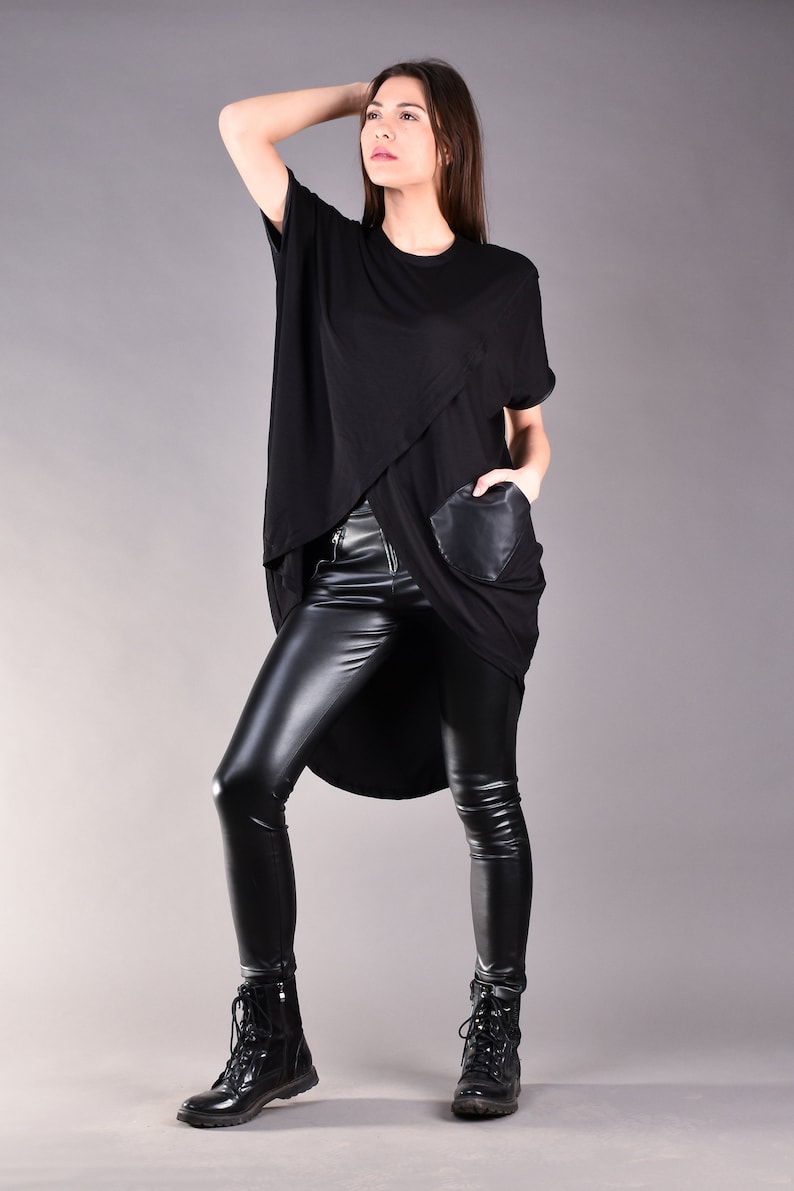 May include: A black, long-sleeved shirt with a high-low hemline and a faux leather pocket. The shirt is paired with black leather leggings and black combat boots.