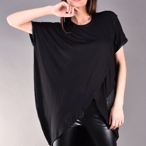 May include: A black, long-sleeved shirt with a high-low hemline and a leather panel on the side. The shirt is worn with black leather pants.