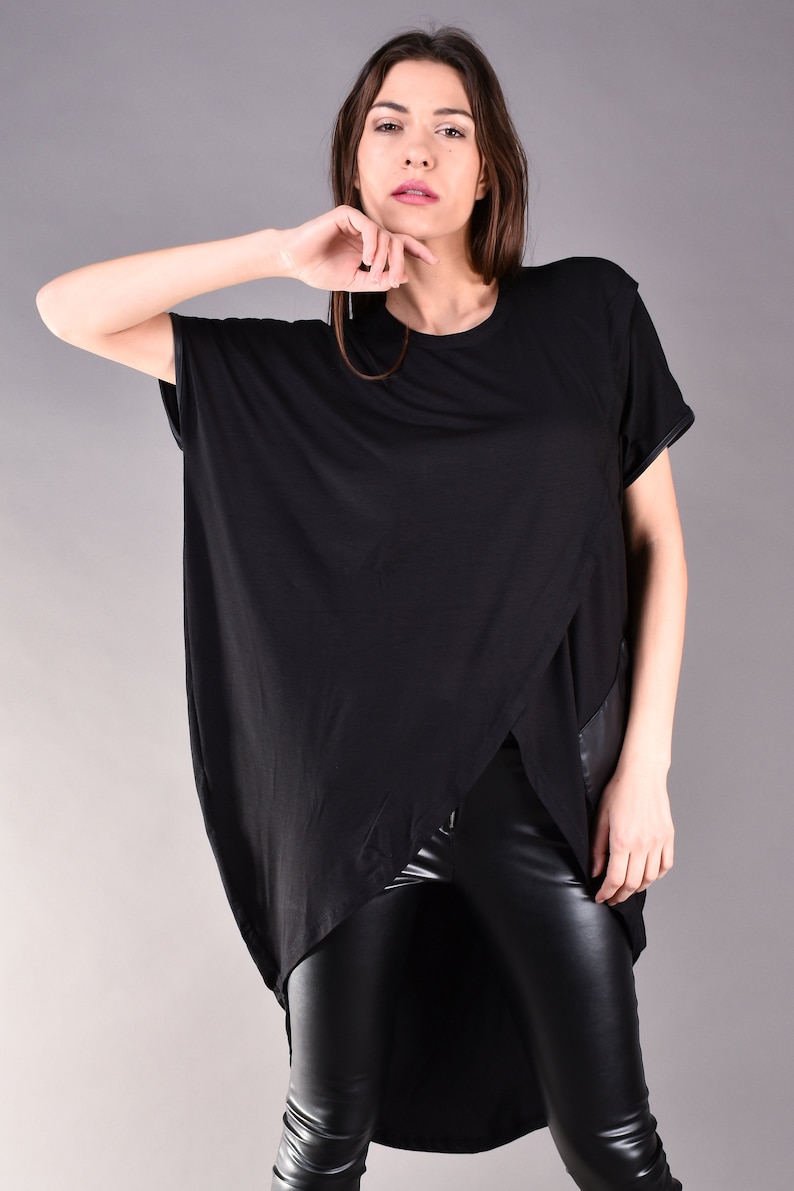 May include: A black, long-sleeved shirt with a high-low hemline and a leather panel on the side. The shirt is worn with black leather pants.