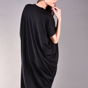 May include: A black, long-sleeved, asymmetrical tunic top with a draped design. The top is made of a soft, flowing fabric.