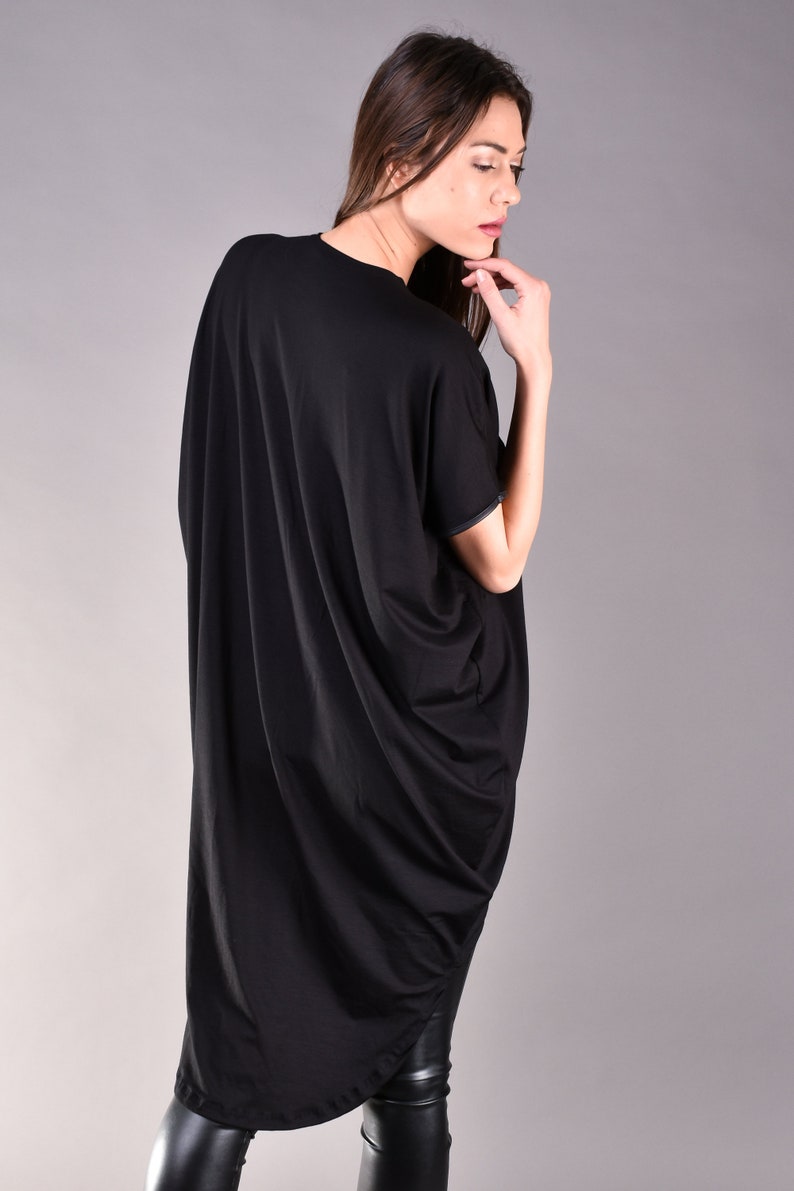 May include: A black, long-sleeved, asymmetrical tunic top with a draped design. The top is made of a soft, flowing fabric.