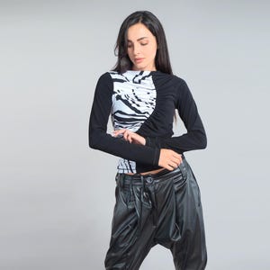 May include: A long-sleeved top with a black and white zebra print design. The top has long black sleeves and a ruched detail on the front. The model is also wearing black leather pants. The outfit is set against a plain gray background.