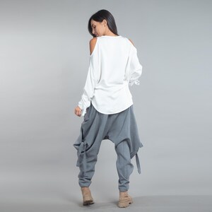 May include: A white, long-sleeved top with open shoulders and grey, loose-fitting trousers. The trousers have a unique design with ties at the sides. The outfit is casual and stylish, suitable for everyday wear.