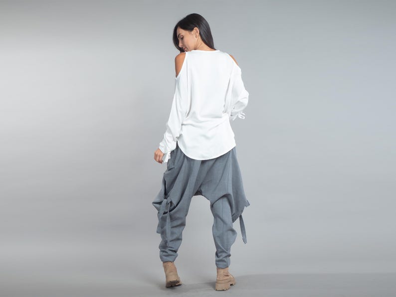 May include: A white, long-sleeved top with open shoulders and grey, loose-fitting trousers. The trousers have a unique design with ties at the sides. The outfit is casual and stylish, suitable for everyday wear.