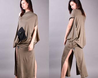 May include: Olive green maxi dress with a unique asymmetrical design. The dress features a draped top with a single sleeve, a black pocket, and a high slit on the skirt. The model is wearing black sandals. The dress is made of a soft, flowing fabric.
