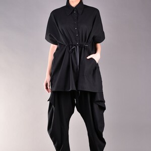 May include: A black, long-sleeved shirt with a button-up collar and a drawstring waist. The shirt is worn over black pants with a loose, flowing fit.