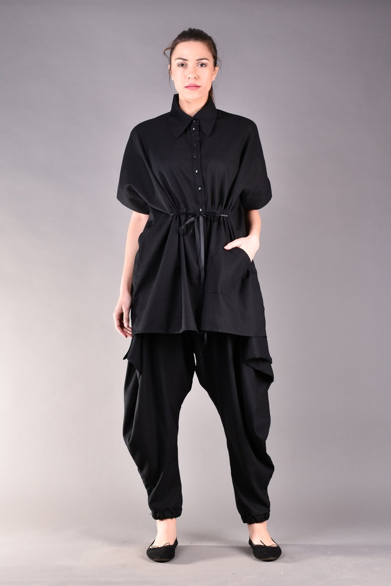 May include: A black, long-sleeved shirt with a button-up collar and a drawstring waist. The shirt is worn over black pants with a loose, flowing fit.