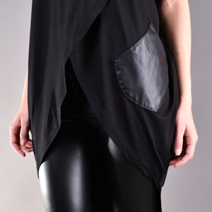 May include: Black long-sleeved shirt with a draped front and a black faux leather pocket. The shirt is paired with black leather leggings.