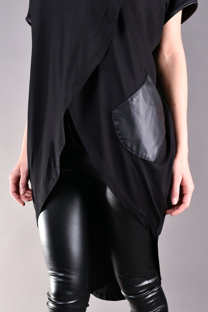 May include: Black long-sleeved shirt with a draped front and a black faux leather pocket. The shirt is paired with black leather leggings.