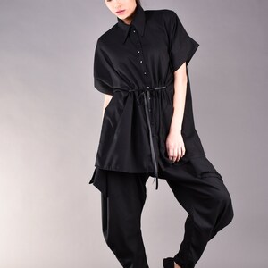 May include: A black, loose-fitting shirt with a collar and a drawstring waist. The shirt is worn with black pants and black flats.