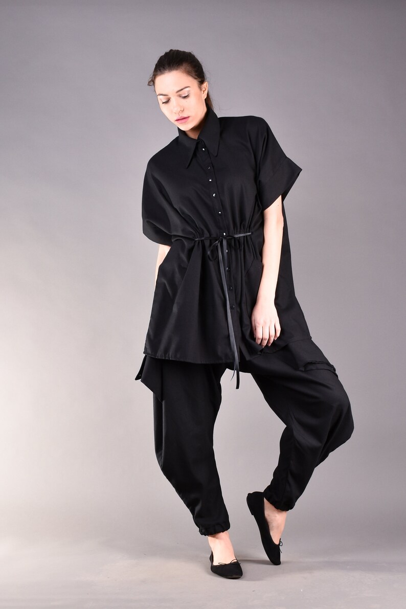 May include: A black, loose-fitting shirt with a collar and a drawstring waist. The shirt is worn with black pants and black flats.