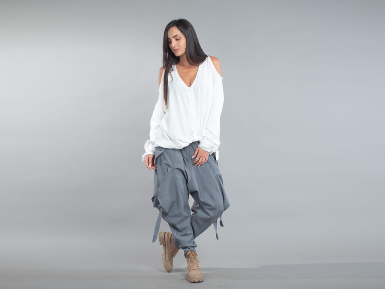May include: A white top with a V-neck and cold shoulder detail, worn with grey cargo trousers with pockets and straps. The outfit is completed with tan boots. The trousers are a similar colour to the top.